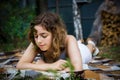 Beautiful teenager girl reading a book lying on blanket on green grass at the forest Royalty Free Stock Photo