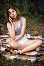 Beautiful teenager girl talking by phone and at the forest. Young girl sitting on blanket at grass Royalty Free Stock Photo