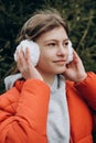 beautiful teenager girl wearing red jacket and earmuffs touching her head and smiling looking aside. vertical waist up