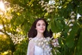 Beautiful teenager girl in white dress with long dark hair at blossoming chestnut tree. Spring blooming and youth Royalty Free Stock Photo