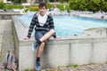 A beautiful teenager walks around the city and sits down to relax at the fountain. Next to him is his backpack, which he always Royalty Free Stock Photo
