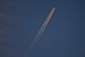 Beautiful telephoto evening view of airplane contrail in orange colors of setting Sun on dark blue background seen over Dublin