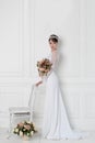 Beautiful tender elegant young girl bride in wedding dress with crown on head in studio on white background with bouquet in hands