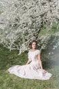 Beautiful tender sweet girl in a pink dress with a hairdo near blossoming tree on a sunny spring day