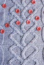 Beautiful texture of a soft warm natural sweater with a knitted pattern of yarn and red small round buttons for sewing. Royalty Free Stock Photo