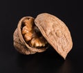 A beautiful textured hard walnut in a shell with half a beautiful walnut kernel inside on a black background.