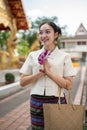 A beautiful Thai woman is standing in a temple in a prayer position with a garland in her hands