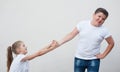 Beautiful thin little caucasian girl pulling with both hands fat strong boy in white shirt and jeans hand on bright background Royalty Free Stock Photo