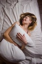 Beautiful thin young woman with long blonde hair in white bed lies hugging a pillow and laughs Royalty Free Stock Photo