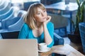 Beautiful thinkful young girl freelancer with blonde bob haircut hair in blue blouse are sitting in cafe and dreaming, having new