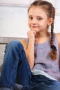 Beautiful thinking cute kid girl sitting on the bench in blue jeans and looking happy. Closeup portrait Royalty Free Stock Photo