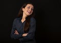 Beautiful thinking toothy laughing business woman with folded arms in blue shirt on black background with empty copy space. Royalty Free Stock Photo