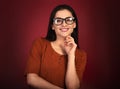 Beautiful thinking toothy smiling happy woman  looking in eye glasses with hand under the face in casual orange t-shirt on red Royalty Free Stock Photo