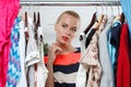 Beautiful thoughtful blonde woman standing inside wardrobe rack