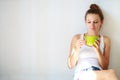 Beautiful thoughtful brunette girl drinks coffee sitting on the floor in an empty room against a white wall background Royalty Free Stock Photo