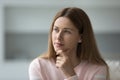 Beautiful thoughtful woman looks aside seated on sofa at home