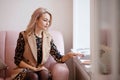 Beautiful thoughtful young woman sits on the couch and looks at the books that lie on the windowsill