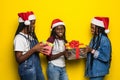Beautiful three african women holding christmas presents isolated on yellow background Royalty Free Stock Photo