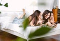 Beautiful three Asian women using app on mobile phone, looking at screen of smart phone, watching photos while lying on bed at Royalty Free Stock Photo