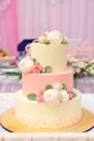 Beautiful three-tiered wedding cake decorated with beige and pink cream and flowers of peony and roses. Close-up Royalty Free Stock Photo