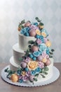 Beautiful three-tiered white wedding cake decorated with colorful flowers roses. Concept of elegant holiday desserts Royalty Free Stock Photo