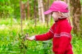 Beautiful three-year-old girl in a red sweater feeds pine nuts with her hands on a titmouse