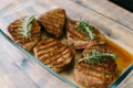 Beautiful toasted steaks in a glass plate on a wooden background, in their own juice and sprigs of rosemary. Royalty Free Stock Photo