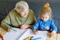 Beautiful toddler girl and grand grandmother drawing together pictures with felt pens at home. Cute child and senior