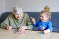 Beautiful toddler girl and grand grandmother playing together pictures lotto table cards game at home. Cute child and