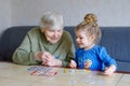 Beautiful toddler girl and grand grandmother playing together pictures lotto table cards game at home. Cute child and
