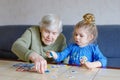 Beautiful toddler girl and grand grandmother playing together pictures lotto table cards game at home. Cute child and