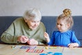 Beautiful toddler girl and grand grandmother playing together pictures lotto table cards game at home. Cute child and