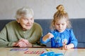 Beautiful toddler girl and grand grandmother playing together pictures lotto table cards game at home. Cute child and