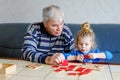 Beautiful toddler girl and grandfather playing together pictures memory table cards game at home. Cute child and senior