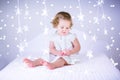 Beautiful toddler girl playing on a white bed between purple Christmas lights Royalty Free Stock Photo