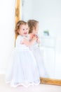 Beautiful toddler girl in white dress next to big mirror