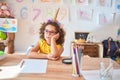 Beautiful toddler wearing glasses and unicorn diadem sitting on desk at kindergarten thinking looking tired and bored with