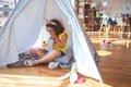 Beautiful toddler wearing glasses and unicorn diadem sitting on the floor at kindergarten shocked covering mouth with hands for Royalty Free Stock Photo