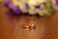 Beautiful toned picture with wedding rings lie on a wooden surface against the background of a bouquet of flowers Royalty Free Stock Photo