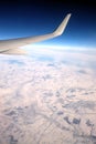 Passenger supersonic plane wing moving high from right to left in blue cloudless sky above snow filds far on the ground Royalty Free Stock Photo