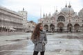 Beautiful tourist girl with long blowing hair in San Marco square in front of the basilica, Venice, Italy. Happy smiling brunette Royalty Free Stock Photo