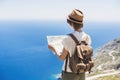 Beautiful tourist woman with backpack holding map. Traveler girl looking for hiking route with sea and mountain at background. Royalty Free Stock Photo