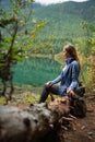 Beautiful tourist woman with backpack siting near azure lake on wooded mountain background. Amazing natural landscape. Concept of Royalty Free Stock Photo