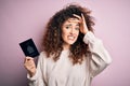 Beautiful tourist woman with curly hair and piercing holding canada canadian passport id stressed with hand on head, shocked with