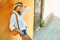 Beautiful tourist woman in straw hat, white shirt smiling and standing by bright orange wall in tourists city. Royalty Free Stock Photo