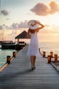 A tourist woman with a white hat walks down a wooden jetty in the Maldives Royalty Free Stock Photo