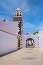 Beautiful traditional brilliant white village, small empty alley with house wall, church tower, archway, blue sky - Teguise,