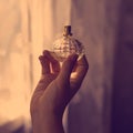 Beautiful translucent glass faceted bottle with fragrance scented toilet water on woman`s hand. Photo filter