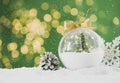 Beautiful transparent Christmas ornament with small fir tree and fairy lights on snow against green background, bokeh effect. Royalty Free Stock Photo