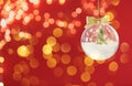 Beautiful transparent Christmas ornament with small fir tree, fairy lights and snow hanging against red background, bokeh effect. Royalty Free Stock Photo